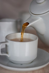 Tea being poured from white modern ceramic teapot into white teacup