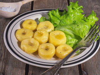 Ready-made potato gnocchi with leaves of fresh leaf lettuce on a ceramic plate with stripes, shot from close range on a plank rustic table.