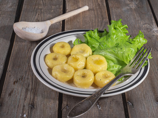 Hot lunch of potato gnocchi with leaves of fresh leaf lettuce on a ceramic plate with stripes, shot from close range on a plank rustic table.