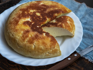 A round cottage cheese casserole with a cut lies on a white plate on a stool, next to a denim napkin.