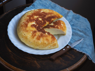 Homemade freshly baked casserole with a cut lies on a white plate on an old chair, next to a denim napkin and a kitchen knife