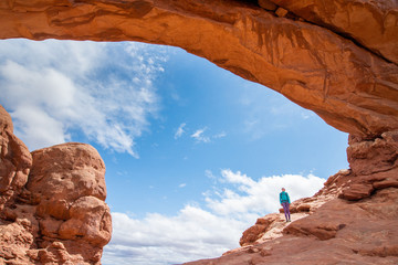 Young woman is standing under the  North Window arch in Arches National Park in Utah. Female tourist is standing under a natural arch in Arches National Park. Travel and adventure concept. © blazekg