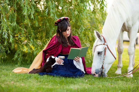 Medieval Princess Reading a Book in the Grass by a Horse