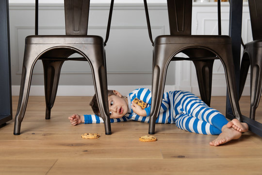 Young boy lying under kitchen table eating a cookie
