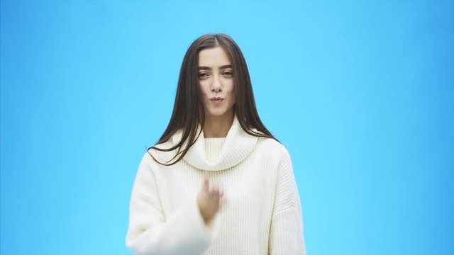 Young beautiful brunette woman on an isolated background. Showing an air kiss with his hands and mouth. Smiling confidently and happily. On a blue background.