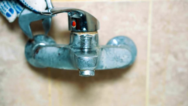 Close-up gloved hands of the plumber uninstalls the faucet. Old faucet is leaking and not working