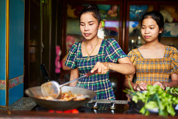 thai mother cooking together with teen daughter in rustic kitchen