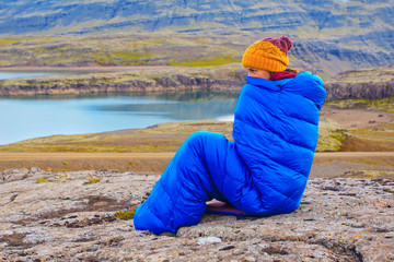 Young woman in warm blue sleeping bag ,  on the stones with northern mass, Iceland