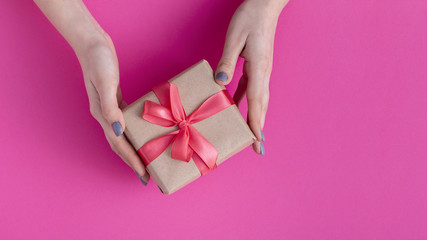 girl holding a present in hands, women with gift box in hands wrapped in decorative craft paper with a tied red ribbon bow on colored cardboard background, top view, concept holiday, love and care