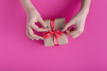 girl wrapping in decorative craft paper a gift and tying a bow, woman with box in hands on colored cardboard background, top view, concept holiday, love and care