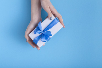 girl holding a beautiful present in hands, women with white gift box with a tied blue ribbon bow in hands on a pastel colored background, top view, concept holiday, love and care