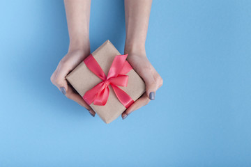 girl holding a present in hands, women with gift box with a tied red ribbon bow in hands on a pastel colored blue background, top view, concept holiday, love and care