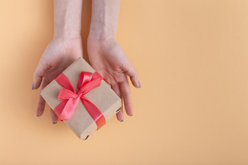 girl holding a present in hands, woman with gift box in hands wrapped in decorative craft paper with a tied red ribbon bow on a pastel colored background, top view, concept holiday, love and care