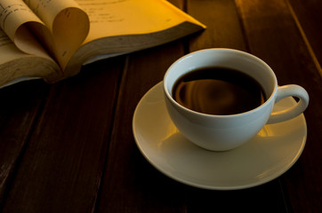 cup of coffee on dark brown wood with heart shape book background