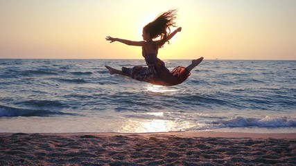 Beautiful girl jumping on the sea coast at sunrise