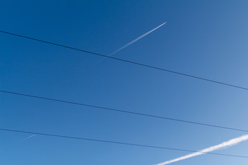 Airplanes in a blue sky with white contrails behind them cross electric wires. Norilsk