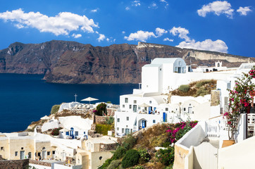 Oia Village, Santorini Cyclade islands, Greece. Beautiful view of the town with white buildings, blue church's roofs and many colored flowers.