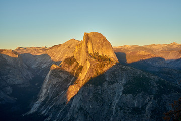 Sun setting over the mountain landscape surrounding the Half Dome at Yosemite National Park, USA, under a blue cloudless sky.