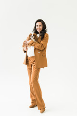Smiling pregnant woman in brown suit holding dog on white background