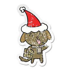 cute distressed sticker cartoon of a dog with christmas present wearing santa hat