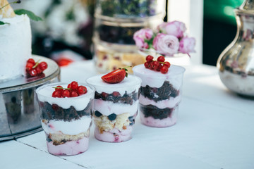Different kinds of delicious sweet desserts and pastries filled with berries and white cream in glasses on the table