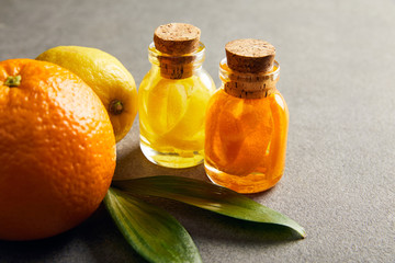 Glass bottles of essential oil with orange and lemon on dark surface