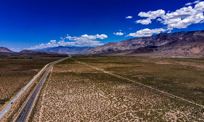 Fototapeta na wymiar Aerial, drone view of Owens Valley and the snowcapped Eastern Sierra Nevada Mountains along California State Highway 395 in the spring with blue sky, white clouds, purple mountains and green flora
