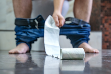 Naklejka premium A man is sitting on the toilet in the bathroom, extends hand to toilet paper. Diarrhea. Stomachache.