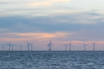 Offshore wind farm turbines on the sea horizon with beautiful pastel sky
