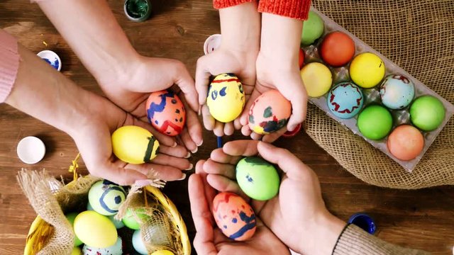The family holds hands with painted eggs over the table with Easter eggs.