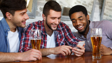 Friends meeting in bar, using smartphone and drinking beer