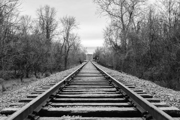 Fototapeta premium Black and white train tracks with a bridge in distance.