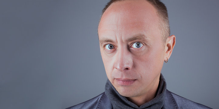 Male model looks inquiringly into the frame on a gray background. Close-up of a male portrait with interrogative emotion. The sensation of a rhetorical question