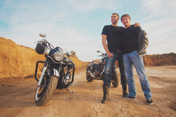 Fototapeta na wymiar Two bikers friends hug near unknown motocycles sandy on road