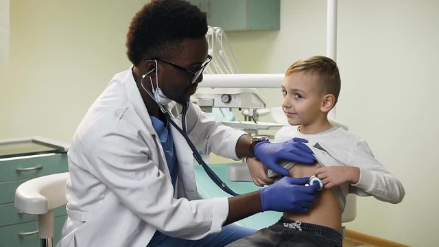 Handsome african doctor checking little boy in the hospital office.