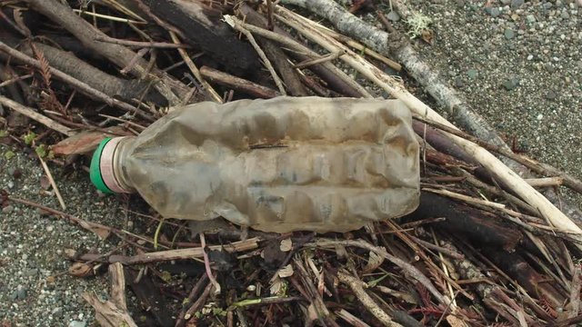 Close-up of a plastic bottle on the beach as the camera pans from left to right.