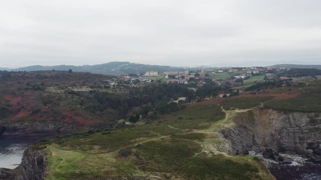 Aerial low drone flight over the tree crones to the little village located on grassy hills; extremely near view from above of winter countryside life; foggy day in Spain north; beautiful rural scene