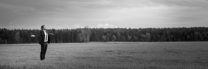 Young businessman in a suit standing in a meadow with his arms wide open