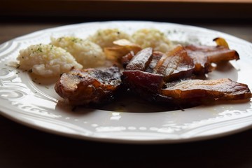 Roasted pork meat in bacon with rice on a white plate