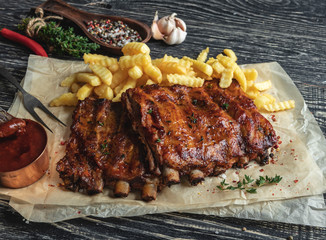 grilled pork ribs with sauce on a cutting board, french fries