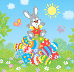 Little Easter Bunny on a pile of colorfully decorated eggs on green grass on a sunny spring day, vector illustration in a cartoon style