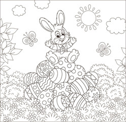 Little Easter Bunny on a pile of colorfully decorated eggs on grass on a sunny spring day, black and white vector illustration in a cartoon style for a coloring book
