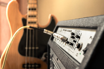 Vintage electric bass plugged into large speaker. Close up of amplifier controls with blur effect on background. Playing bass in home.