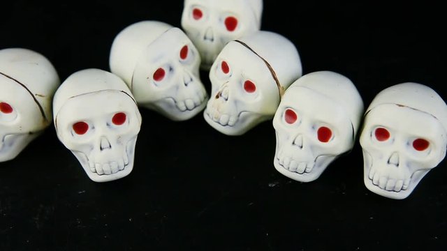 human hand put many white chocolate candies in skeleton skull shape with red eyes on black background