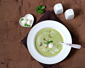 Cream of green pea soup, sprinkled with pumpkin seeds, in a white plate. Served with mozzarella cheese. Top view.