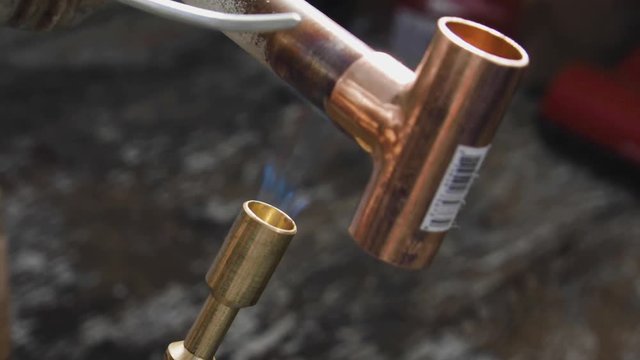 Solder being melted on a copper tee connection while it's being heated by a propane blow torch. Extreme closeup.