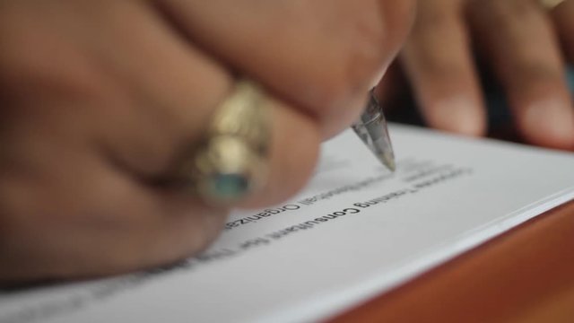 A male hand edits a printed document with a pen on a wooden table.