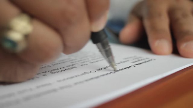 A male hand edits a printed document with a pen on a wooden table.