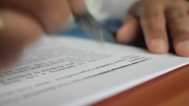A male hand edits a printed document with a pen on a wooden table.