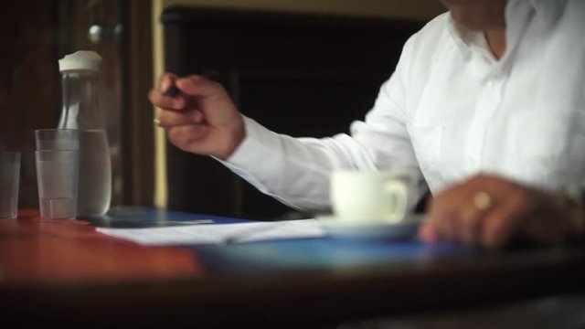 A male hand edits a printed document with a pen on a wooden table.
